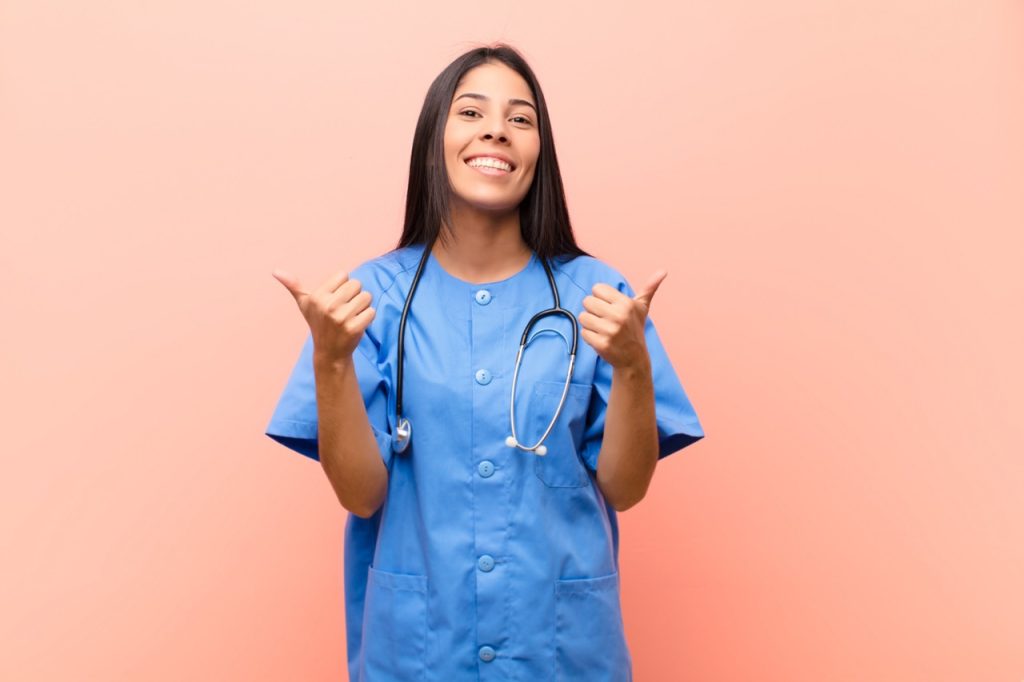 CNA smiling with both thumbs up in front of pink background