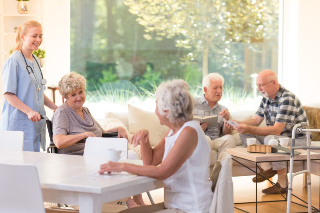 Group of seniors spending free time in bright community room with big window at assisted living facility